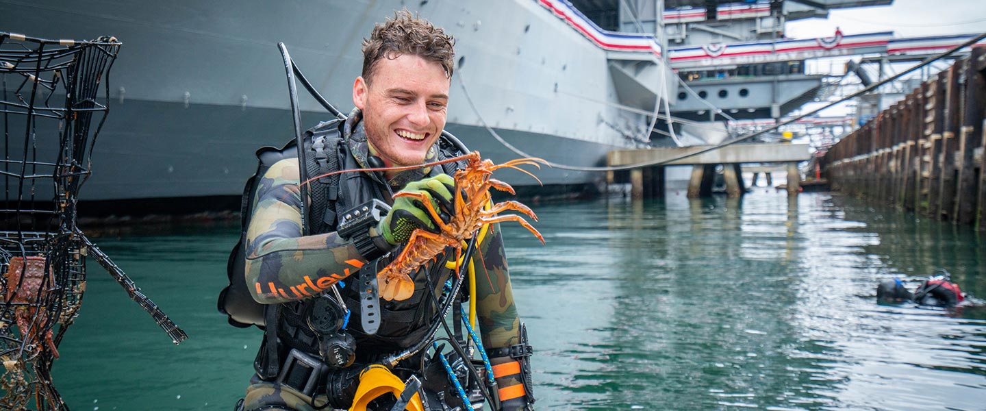 Scuba Diving YouTuber Jake aka dallymd holds a live lobster retrieved during a dive near a Navy ship
