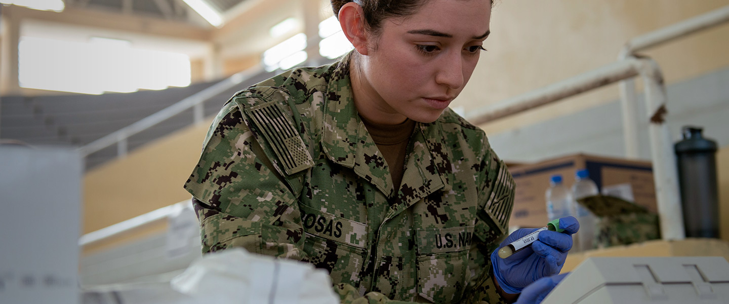 A Navy medical laboratory technician exams blood samples and inputs data in a laboratory environment