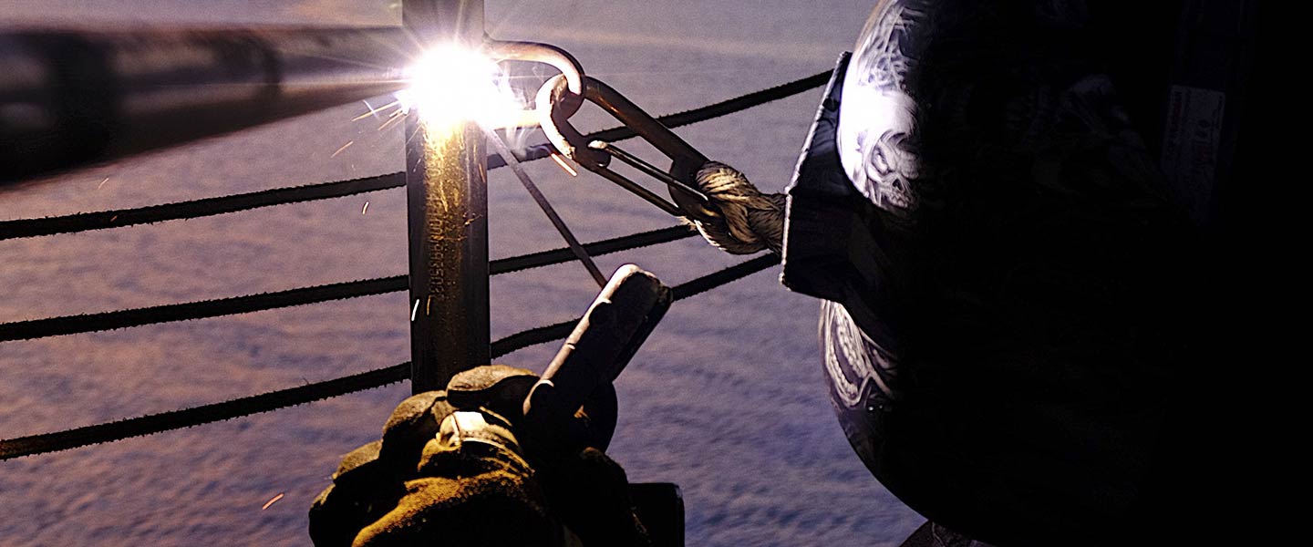 A United States Navy Hull Maintenance Technician sailor stick-welds a railing aboard the USS Germantown.